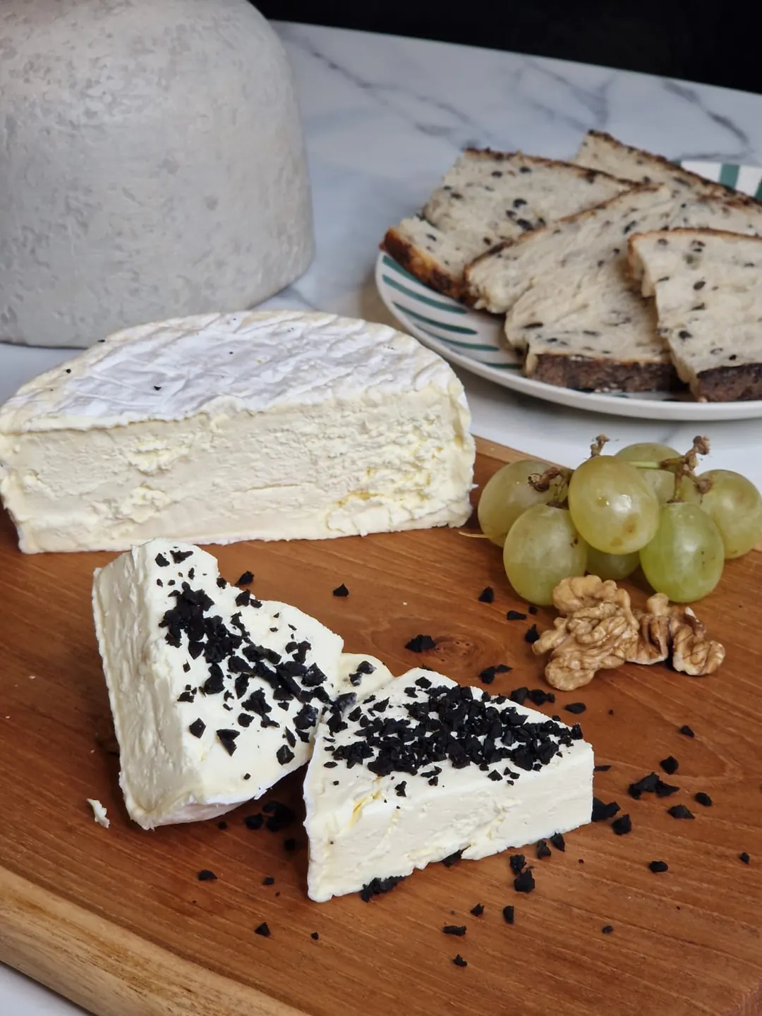 Käse auf einem Brett mit Brot, einer Weintraube und Walnüssen.