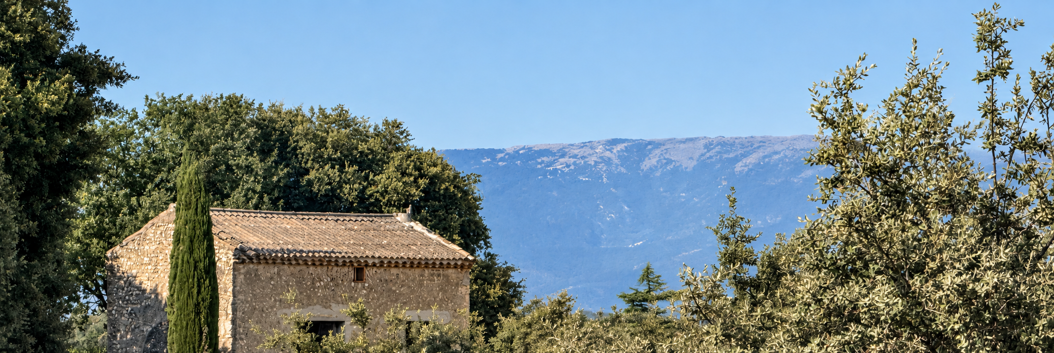 Une maison en pierre entourée d’arbres, avec les montagnes en arrière-plan