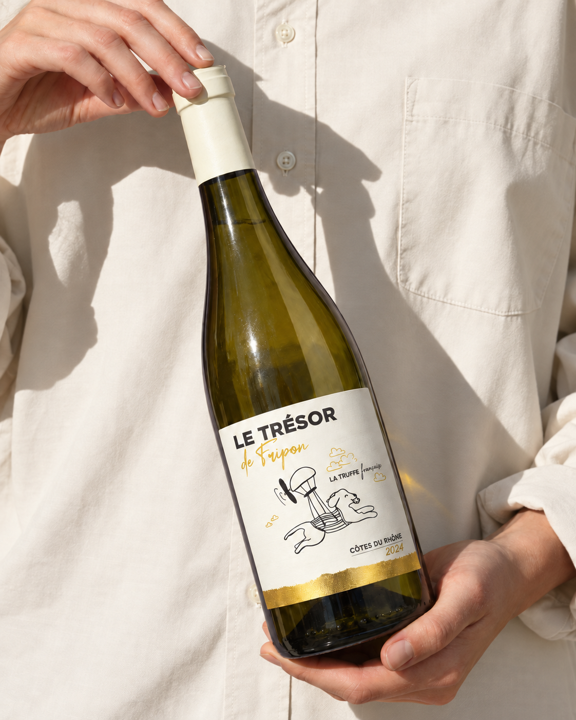 Une bouteille de vin blanc Le Trésor de Fripon tenue dans les mains